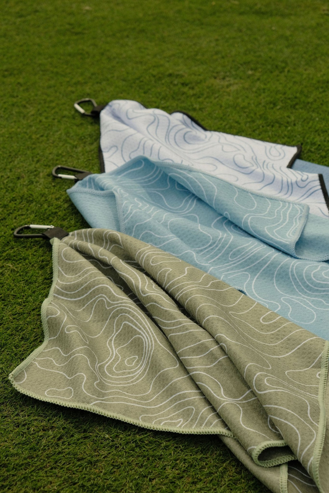 Folded golf towels in green, blue, and white on a grassy background