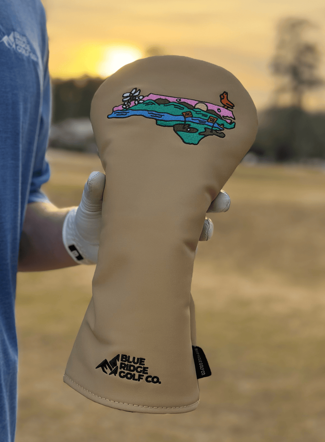 Beige golf club head cover with colorful design and 'Blue Ridge Golf Co.' branding, held by a person.