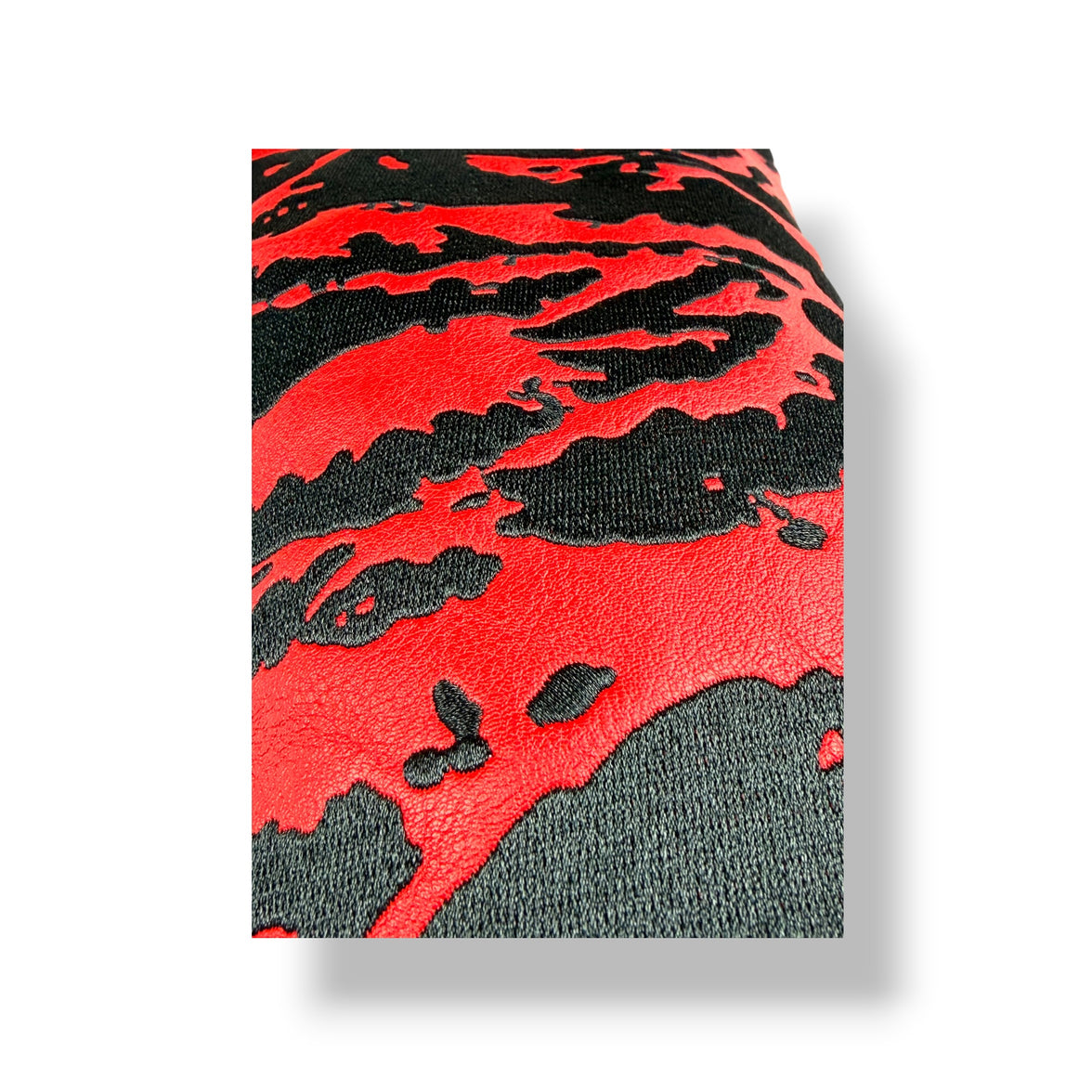 A close-up of a textured material featuring a bold red and black abstract pattern, shown as a folded swatch on a white background with a soft drop shadow.