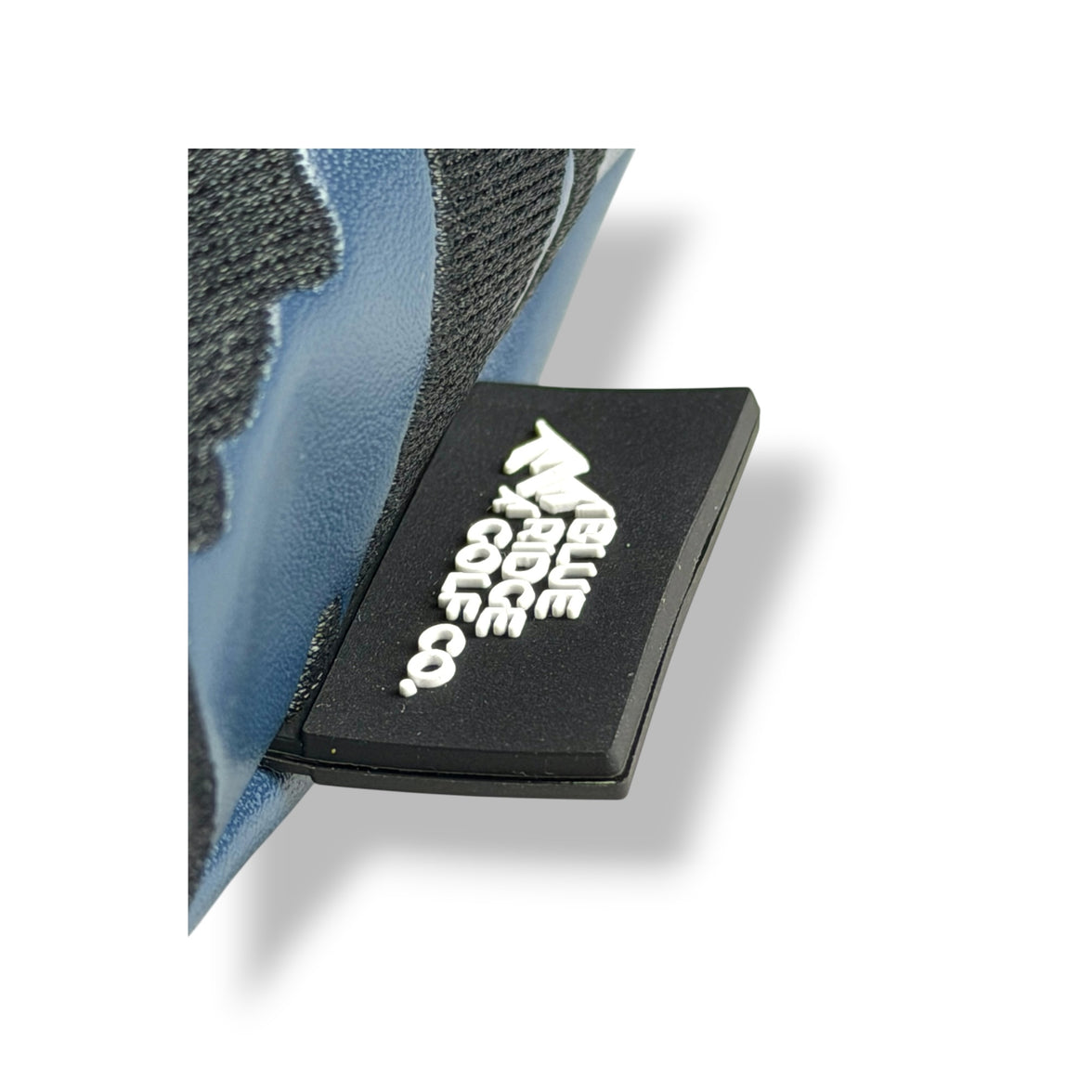 A close-up of a black rectangular patch with white stylized text and logo, attached to a blue and dark gray textured shoe or boot on a white background.