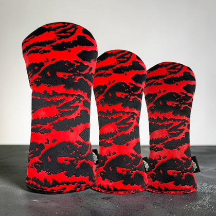 Three golf club headcover sleeves with a bold red and black abstract camouflage pattern, arranged in descending size order on a dark surface against a light gray background.