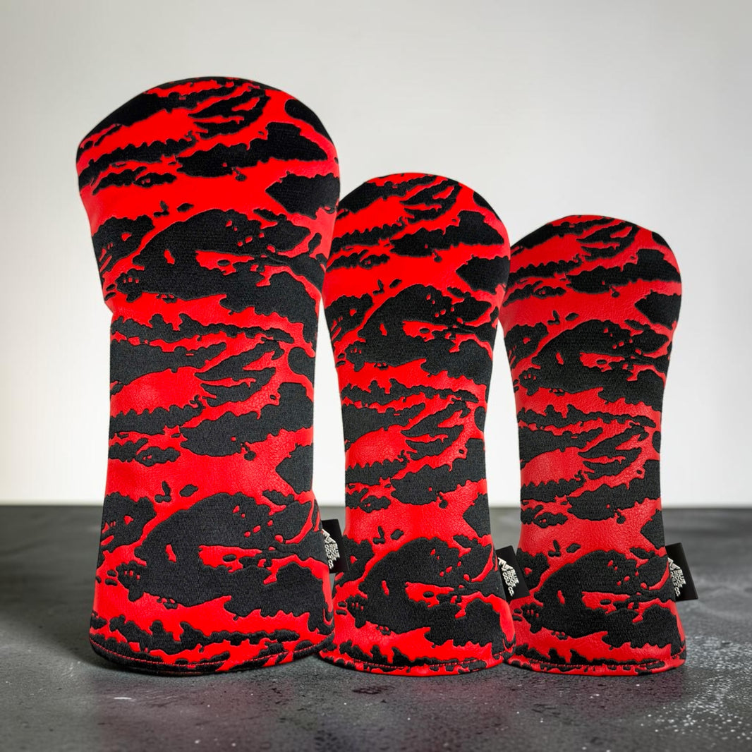 Three golf club headcover sleeves with a bold red and black abstract camouflage pattern, arranged in descending size order on a dark surface against a light gray background.