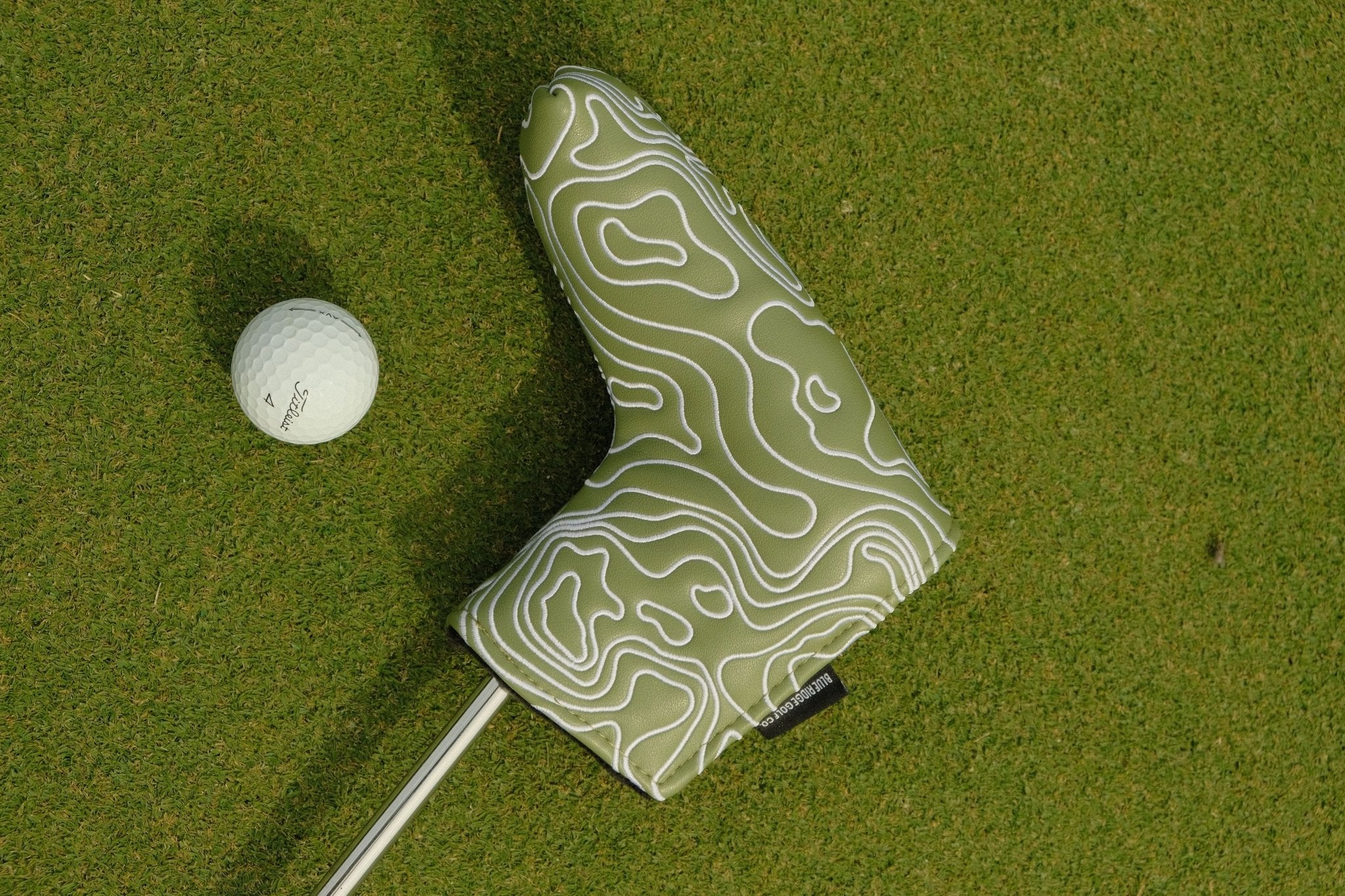 Golf club head cover with topographic design on a green golf course